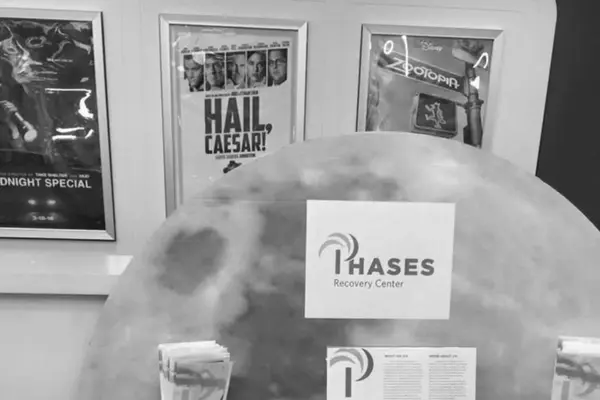 A circular display with the logo of Phases Recovery Center in front of framed movie posters, featuring "HAIL, CAESAR!" and "Zootopia"